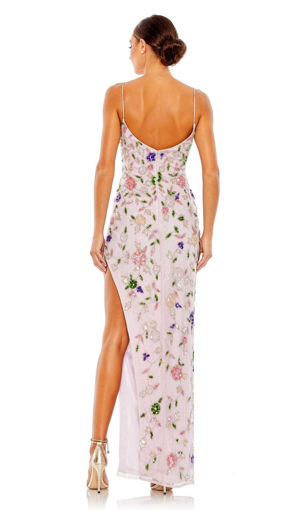 A woman faces away, wearing the Mac Duggal Long Formal Dress 10893—a floor-length, light pink floral beaded gown with thin straps and a high slit. She finishes the look with metallic heels and a low bun.